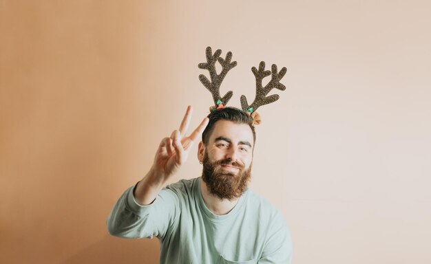 Foto junger hipster-bartmann in stilvoller weihnachtskleidung, der spaß mit einem bunten abnehmbaren hintergrund hat. konzept für das neue jahr. spaß und spielerisches konzept. zeigen von kopienraum mit smartphone,