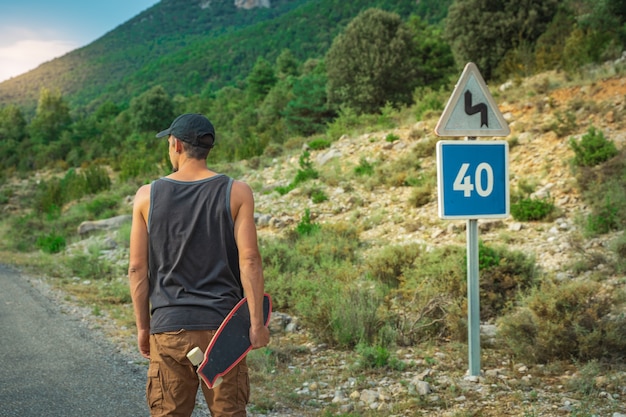 Junger Hipster, der ein cooles Longboard in der Hand hält