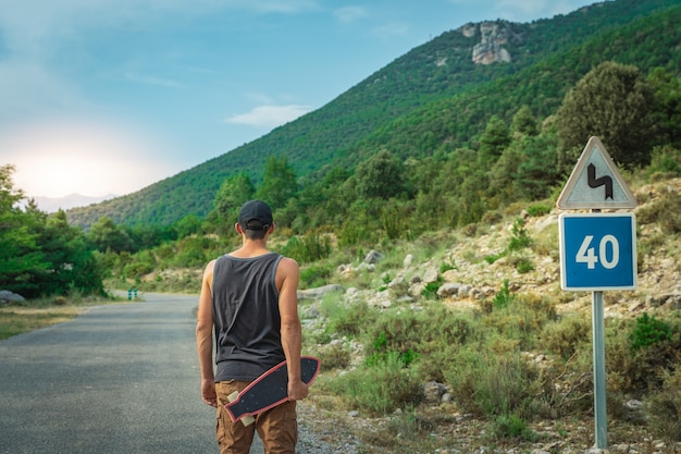 Junger Hipster, der ein cooles Longboard in der Hand hält