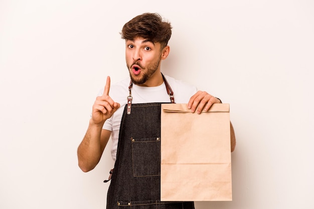 Junger hispanischer Angestellter, der eine Tasche zum Mitnehmen isoliert auf weißem Hintergrund hält und ein Ideeninspirationskonzept hat