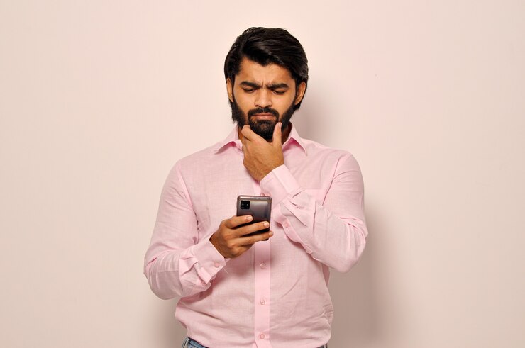 Junger hispanischer Geschäftsmann mit Smartphone mit ernstem Gesichtsausdruck Denkender Blick