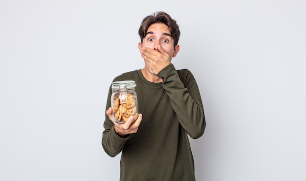 Junger hispanischer Mann, der den Mund mit den Händen mit einem schockierten bedeckt. Cookies-Konzept