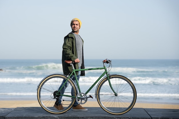Junger hispanischer Mann, der mit einem Fahrrad am Meer aufwacht