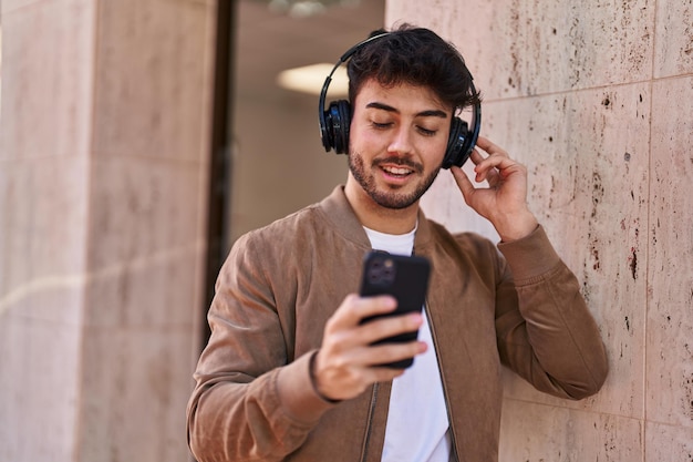 Junger hispanischer Mann, der selbstbewusst lächelt und Musik auf der Straße hört