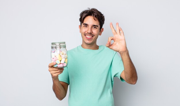 Junger hispanischer Mann, der sich glücklich fühlt und Zustimmung mit okayer Geste zeigt. Gelee Bonbons Konzept