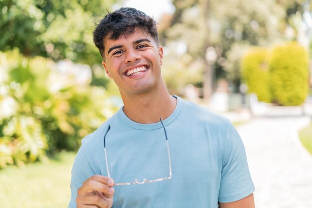 Foto junger hispanischer mann im freien mit brille und glücklichem gesichtsausdruck