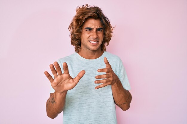 Foto junger hispanischer mann in lässiger kleidung, angewiderter gesichtsausdruck, unzufrieden und ängstlich, macht ekelgesicht, weil abneigungsreaktion mit erhobenen händen