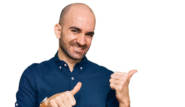 Junger hispanischer Mann in lässiger Kleidung, der mit der Hand und den Daumen nach oben auf den Rücken zeigt und selbstbewusst lächelt
