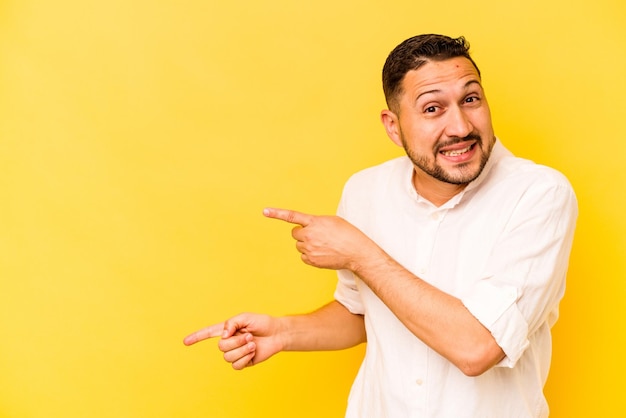 Junger hispanischer Mann isoliert auf gelbem Hintergrund aufgeregt mit Zeigefingern weg zeigend