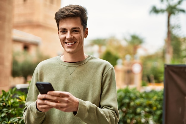 Junger hispanischer Mann lächelt glücklich mit Smartphone in der Stadt.