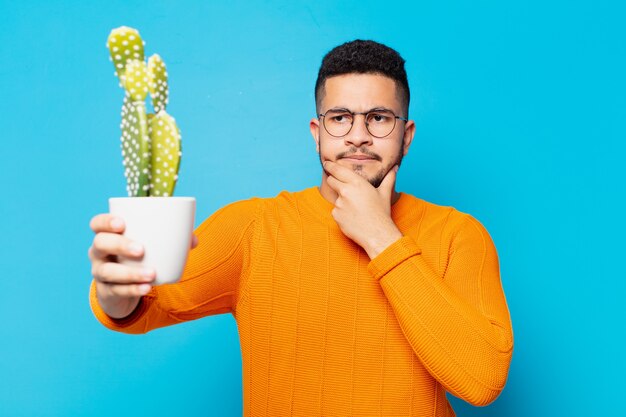 Junger hispanischer Mann mit denkendem Ausdruck und hält einen Kaktus