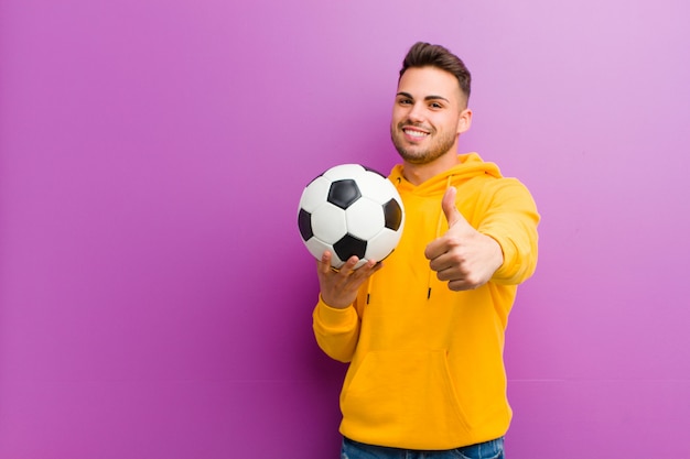 Junger hispanischer Mann mit einem Fußball gegen Purpur