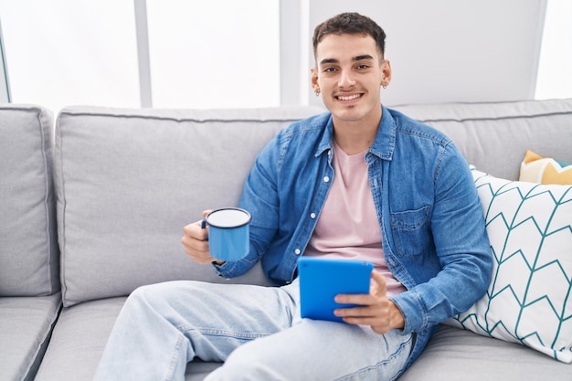 Junger hispanischer Mann trinkt Kaffee mit Touchpad zu Hause