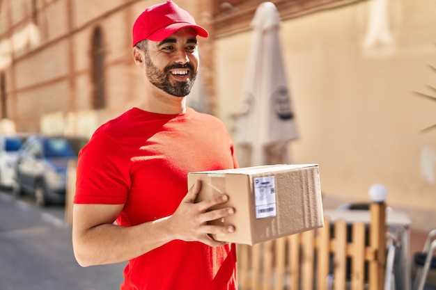 Junger hispanischer Mannkurier, der Paket an der Straße hält