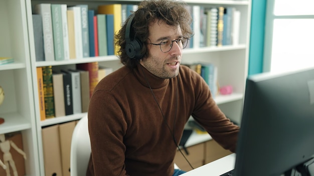 Junger hispanischer Student nutzt Computer und Kopfhörer und studiert an der Bibliotheksuniversität