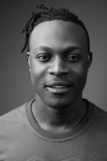 junger hübscher afrikanischer Mann aus Kenia gegen graue Wand in Schwarzweiss