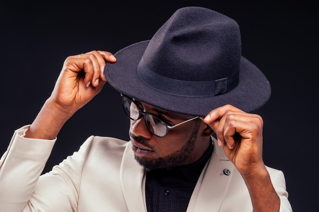 Junger hübscher afroamerikanischer melancholischer Junge in einer weißen Jacke und Brille auf schwarzem Hintergrund im Studio. Geheimnis und Trauer