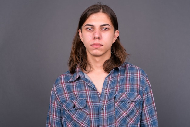 junger hübscher androgyner Hipster-Mann mit langen Haaren gegen graue Wand