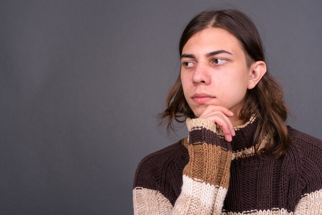 junger hübscher androgyner Mann mit langen Haaren bereit für Winter gegen graue Wand