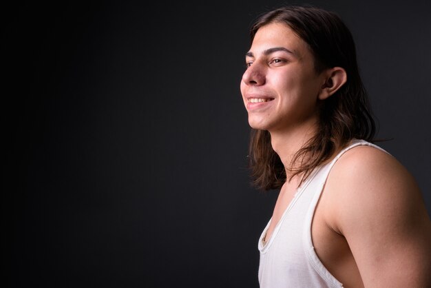 junger hübscher androgyner Mann mit langen Haaren gegen graue Wand