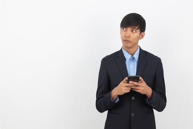 Junger hübscher asiatischer Geschäftsmann, der Smartphone spielt und denkt