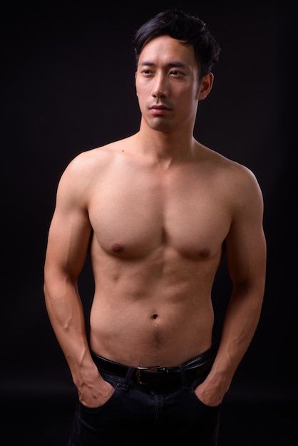 Junger hübscher asiatischer Mann hemdlos auf schwarzer Wand