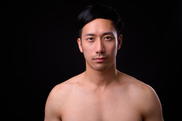 Junger hübscher asiatischer Mann hemdlos auf schwarzer Wand