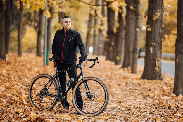 Junger hübscher athletischer Mann, der mit Fahrrad im Herbstpark steht