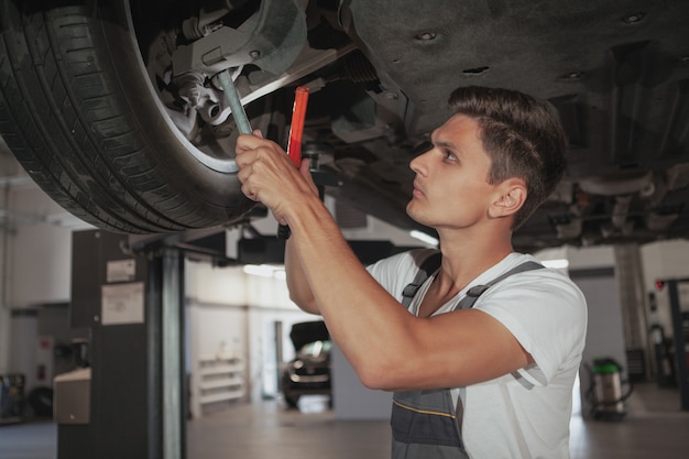 Junger hübscher Automechaniker, der Fahrzeug in seiner Garage repariert