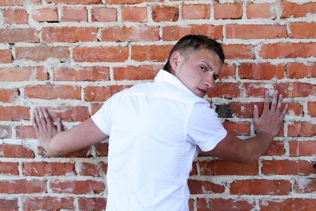 Junger hübscher blonder Kerl in einem weißen Hemd steht nahe einer alten Backsteinmauer