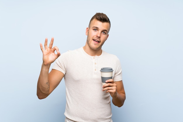 Junger hübscher blonder Mann, der heißen Tasse Kaffee hält