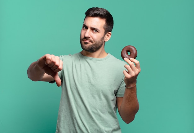 Junger hübscher blonder Mann mit einem Schokoladenkrapfen. Frühstückskonzept