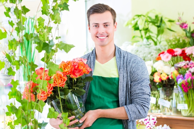 Junger hübscher Florist, der Blumen und Blumensträuße im Geschäft verkauft