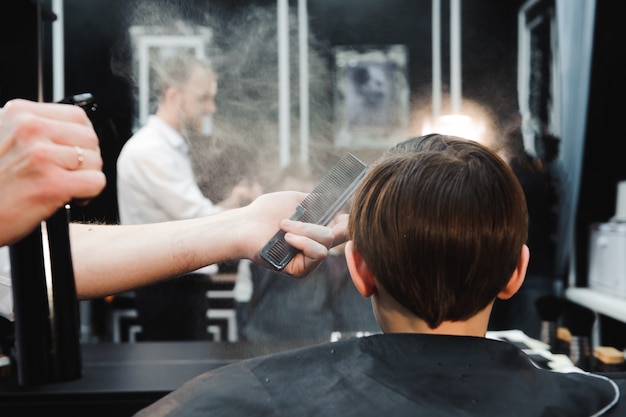 Junger hübscher friseur, der haarschnitt vom jungen im friseursalon macht