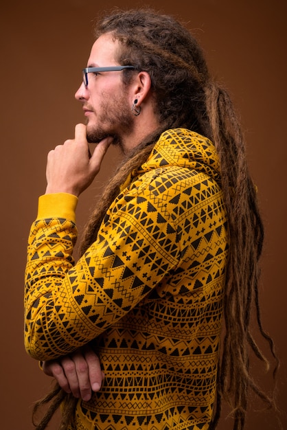 Junger hübscher hispanischer Mann mit Dreadlocks gegen braunen Hintergrund