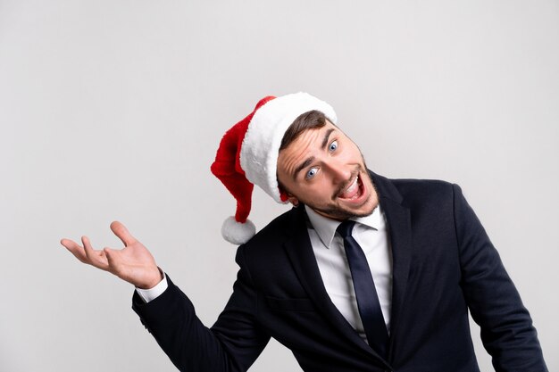 Junger hübscher kaukasischer Kerl im Geschäftsanzug und in der Weihnachtsmannmütze