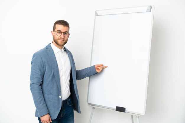 Junger hübscher kaukasischer Mann lokalisiert auf weißer Wand, die eine Präsentation auf weißer Tafel gibt