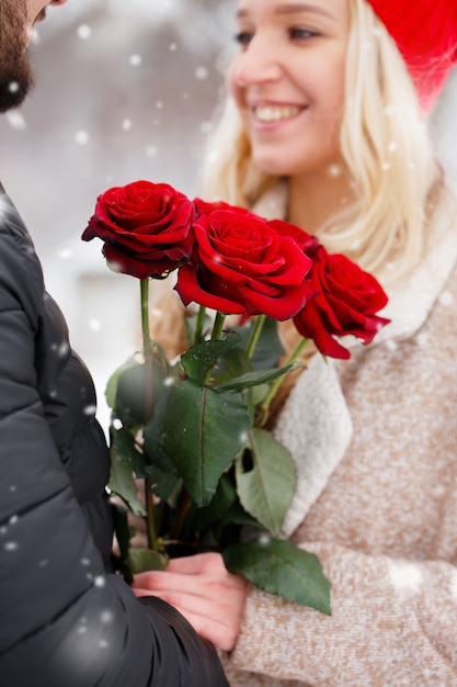 Junger hübscher Kerl, der einem Mädchen einen Strauß Rosen am Valentinstag gibt