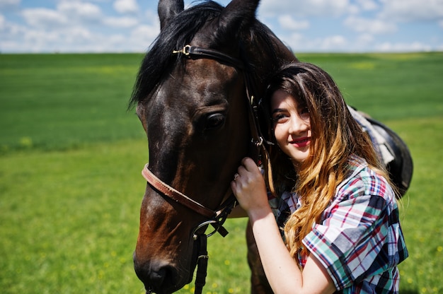 Junger hübscher Mädchenaufenthalt mit Pferd auf einem Feld am sonnigen Tag.