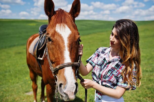 Junger hübscher Mädchenaufenthalt mit Pferd auf einem Feld am sonnigen Tag.