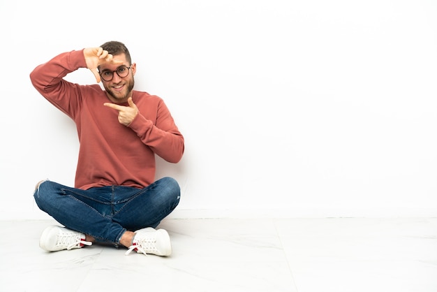 Junger hübscher Mann, der auf dem Boden sitzt, der Gesicht fokussiert