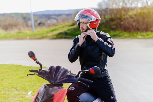 Junger hübscher Mann, der auf seinem Fahrrad mit Helm in seinen Händen sitzt.