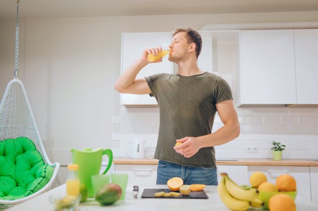 Junger hübscher Mann, der frischen Orangensaft in der Küche trinkt. Gesundes Essen.