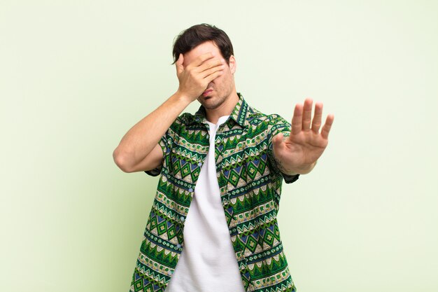 Junger hübscher Mann, der Gesicht mit Hand bedeckt und andere Hand vorne legt, um Kamera zu stoppen, Fotos oder Bilder ablehnend