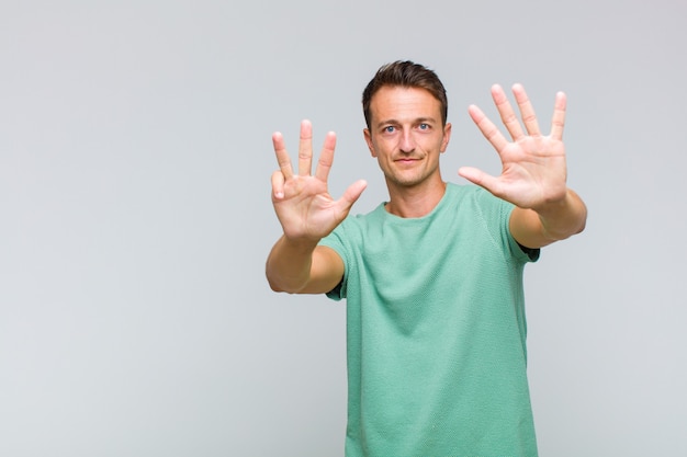 Junger hübscher Mann, der lächelt und freundlich schaut, Nummer neun oder neun mit der Hand vorwärts zeigend, herunterzählend