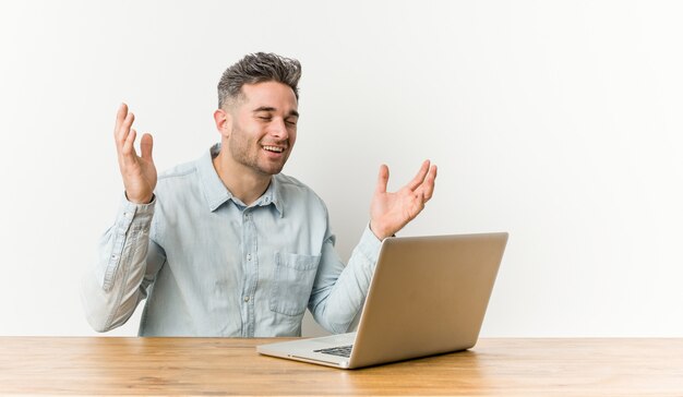 Junger hübscher Mann, der mit seinem Laptop arbeitet, lacht freudig viel