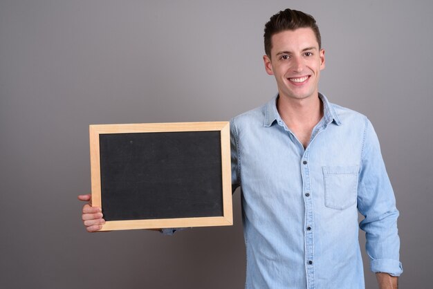 junger hübscher Mann, der Tafel auf Grau hält