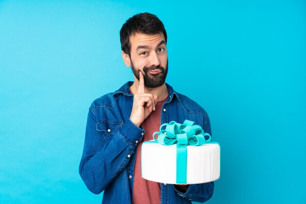 Junger hübscher Mann mit einem großen Kuchen über Blau und schauende Front