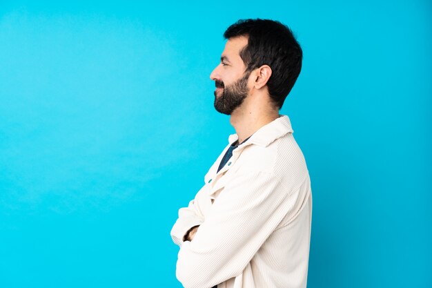 Junger hübscher Mann mit weißer Cordjacke über isolierter blauer Wand in seitlicher Position