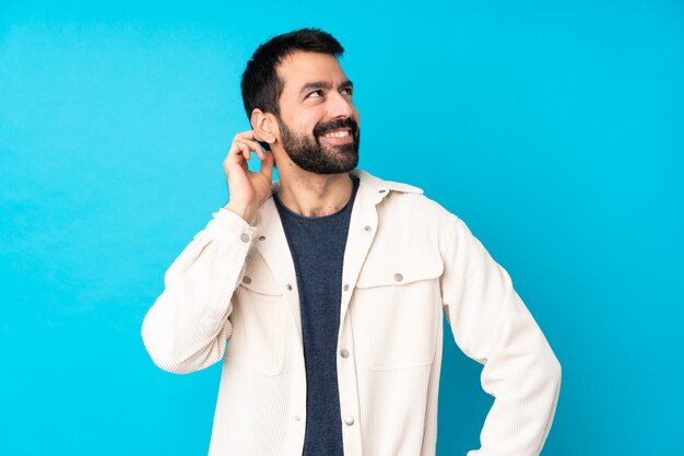 Junger hübscher Mann mit weißer Kordjacke über isolierter blauer Wand, die eine Idee denkt